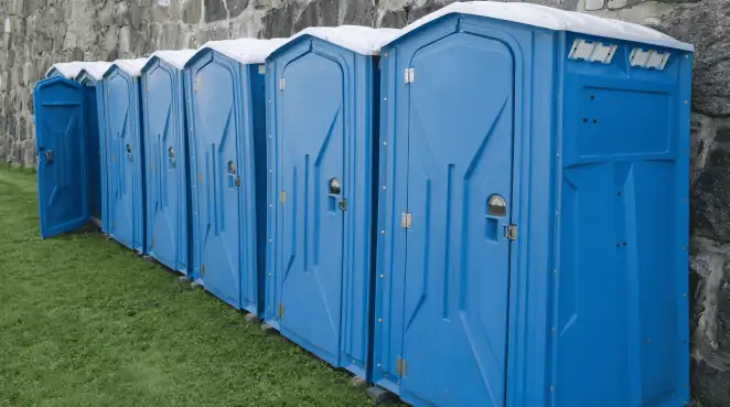 Row of blue portable toilets lined up on grass against a stone wall for event sanitation in Myrtle Beach, SC