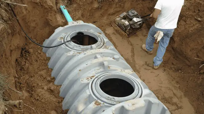 Septic tank installation showing a technician compacting soil around a new poly septic tank in an excavation pit in Myrtle Beach, SC